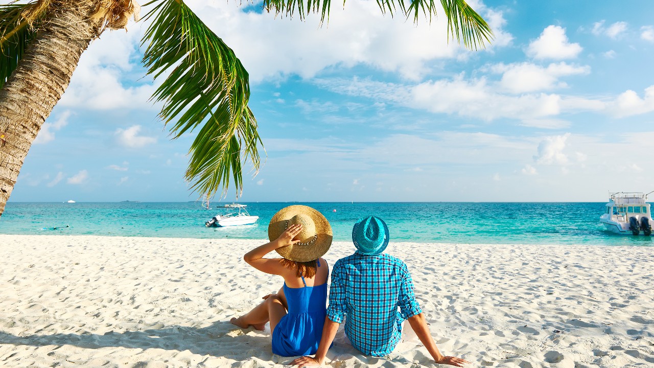 Một cặp đôi ngồi trên bãi biển; hình ảnh được sử dụng cho trang Ưu đãi du lịch và nghỉ dưỡng của Thẻ Thanh Toán Quốc Tế